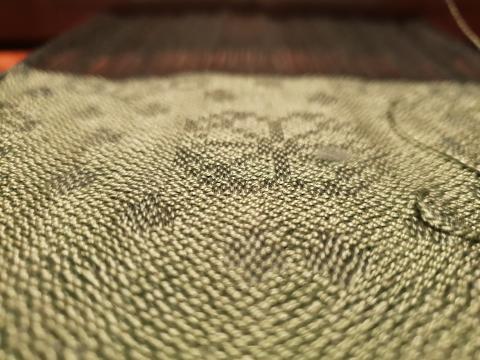 Close up of dark abd light green damask cloth with a circle made of dots and a rise motif with the circle