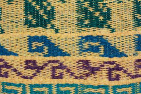 A cloth with a yellow background from bottom to top teal fretts, purple ivyu, blue waves, and green leaves motifs.
