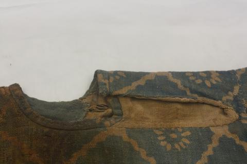 Close up of the neck line which is round with a slit cut down the arm, the hem is finished with similar cloth sewn down as tape over the cut hem.